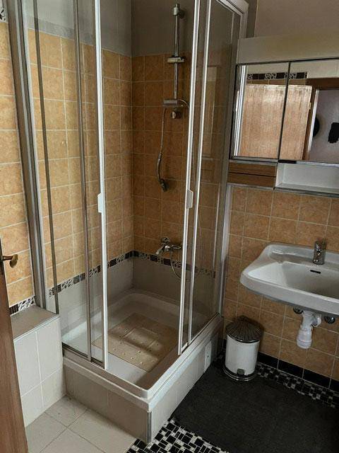 Badezimmer mit Duschkabine, Waschbecken und gemusterten Fliesen im 80er-Jahre-Stil.