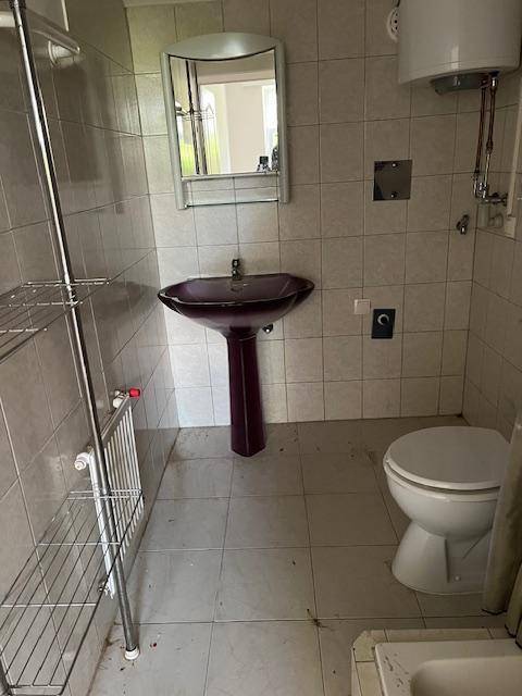 Badezimmer mit Fliesenboden, Waschbecken, Toilette und einem Wandspiegel.