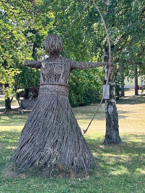 Dekorative Figur aus Weidenzweigen in einer grünen Parkanlage mit Bäumen.