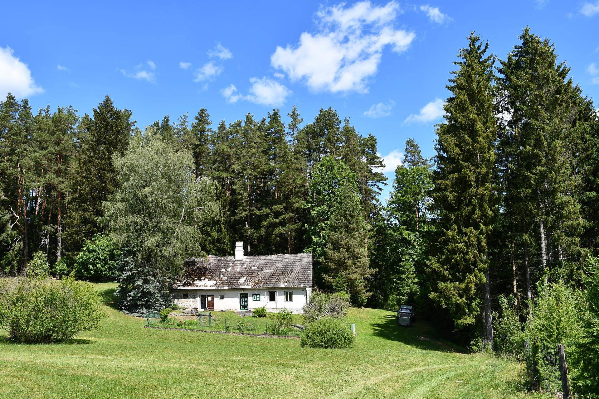 Haus in sonniger Lage, umgeben von weiten Wiesen und einem dichten Wald.