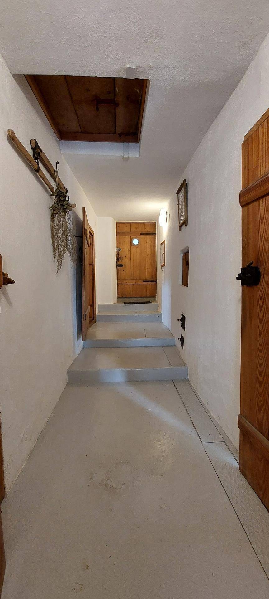 Langer Flur mit weißen Wänden, Holztüren und einer Treppe, die zu weiteren Räumen führt.