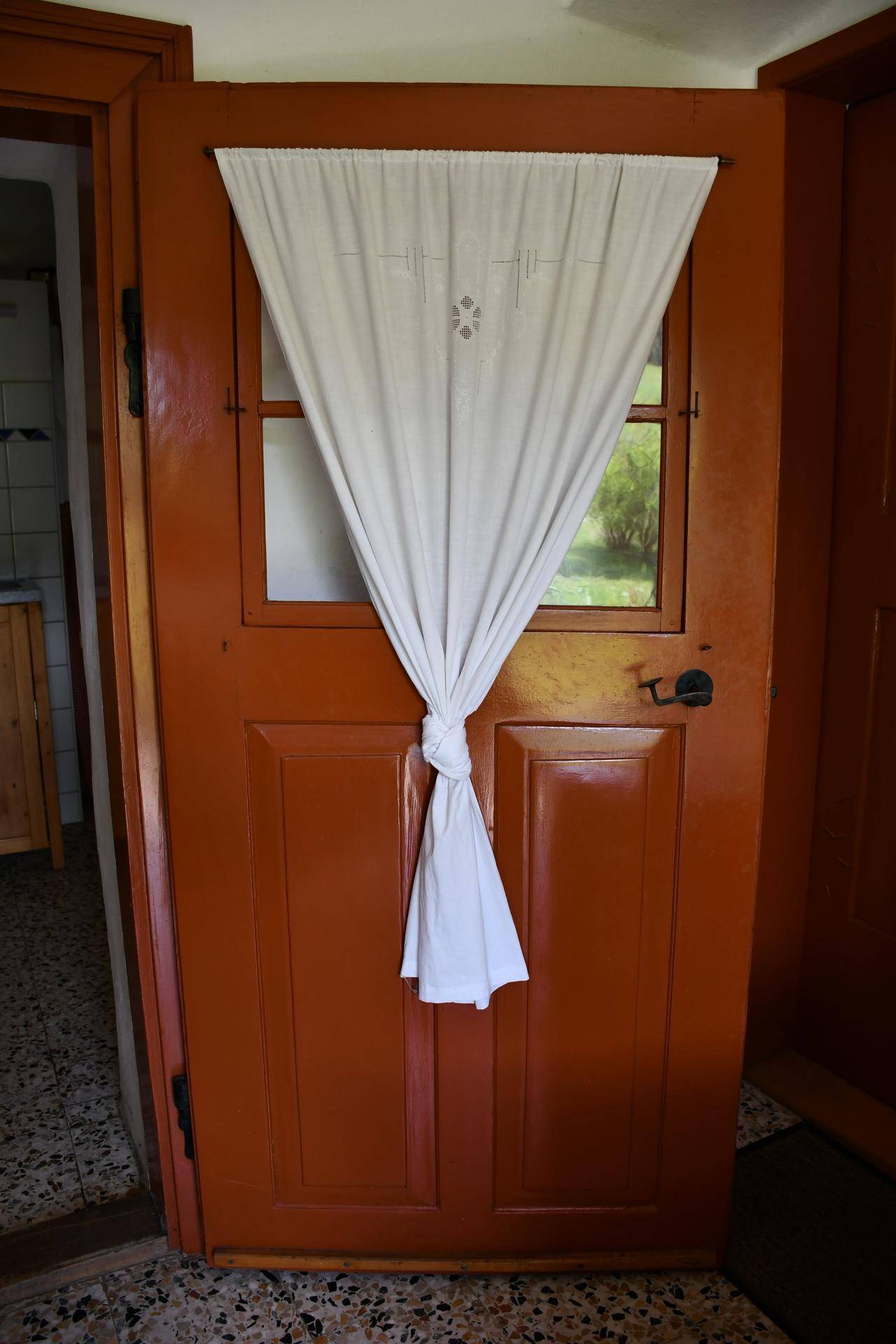 Eine rustikale Holztür mit einem kleinen Fenster, verziert mit einem einfachen Vorhang.
