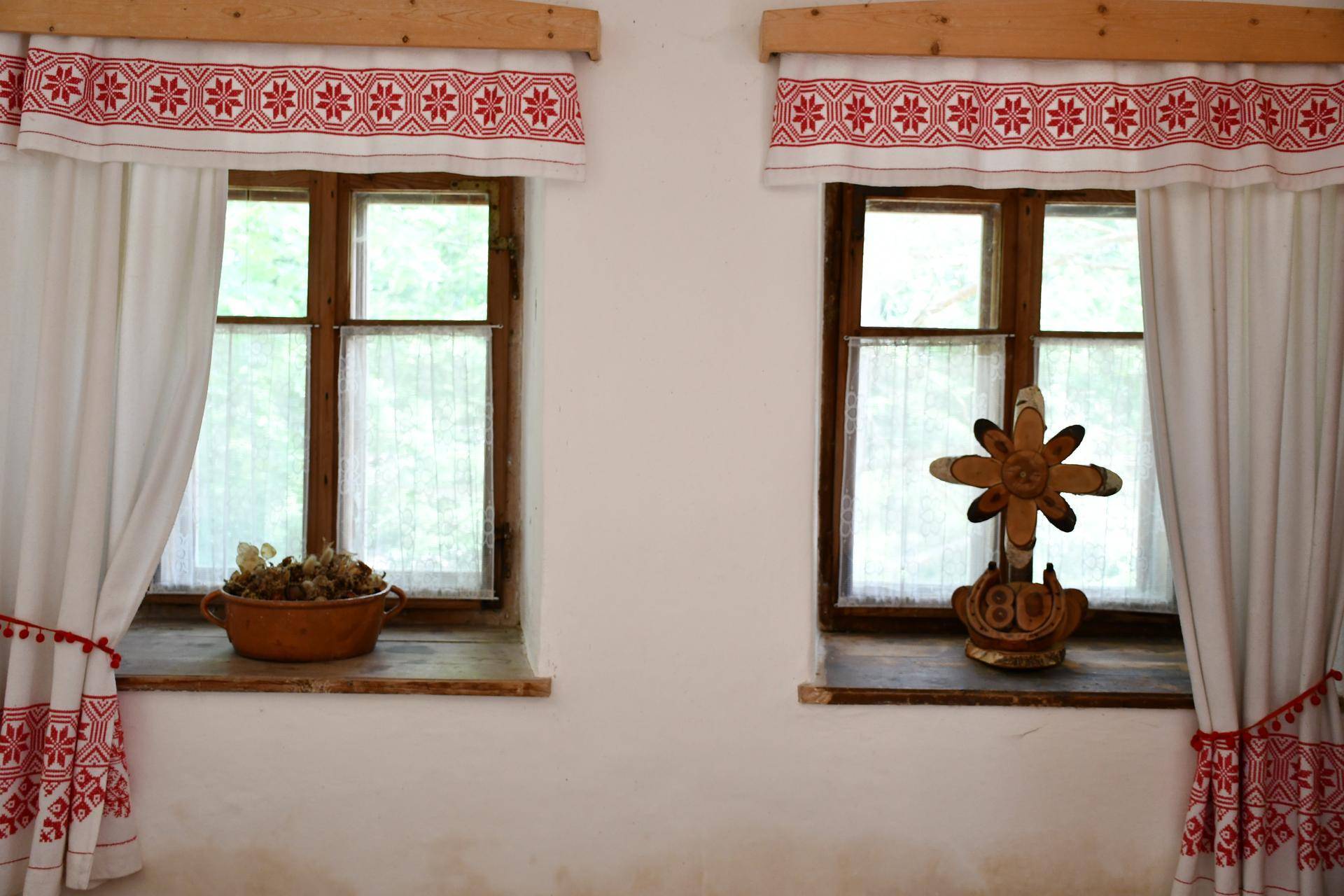Zwei Fenster mit traditionellen rot-weißen bestickten Vorhängen und rustikalen Holzfensterbänken, die Gemütlichkeit ausstrahlen.