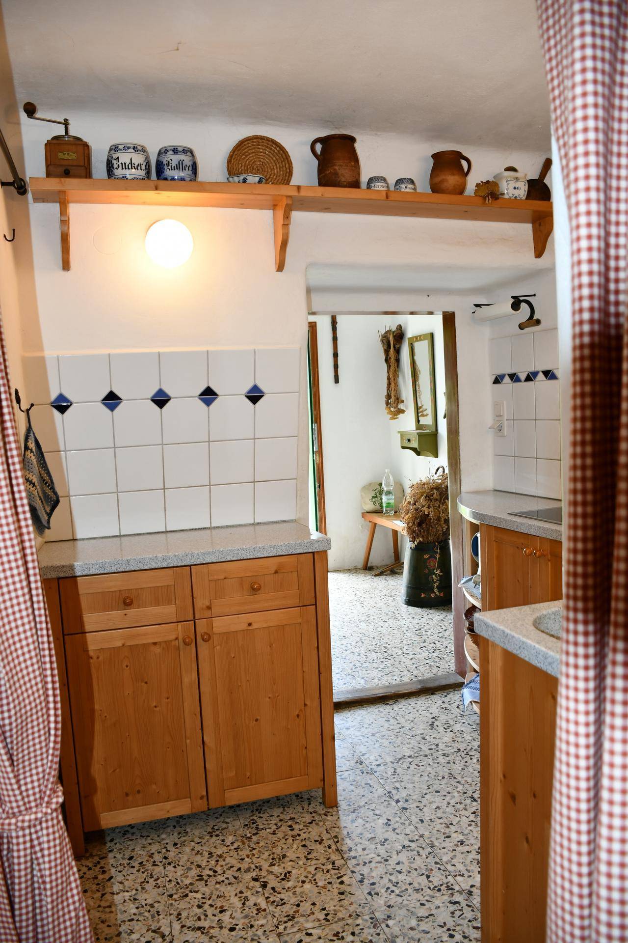 Rustikale Küche mit Holzschränken, gefliesten Wänden und einem Durchgang zu einem weiteren Raum.