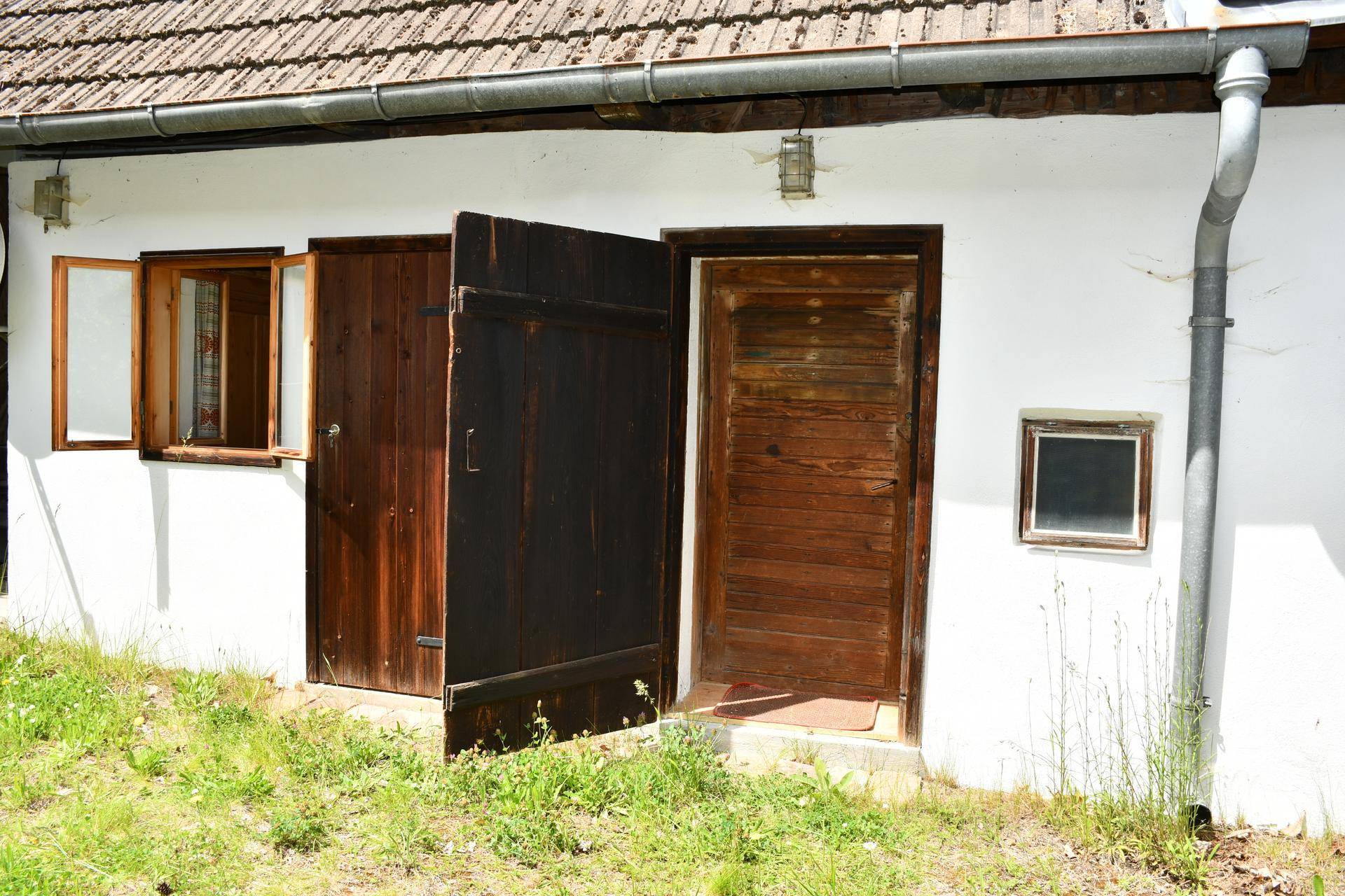 Weiße Hausfassade mit rustikalen Holztüren und Fenstern, die zu einem grünen Außenbereich führen.