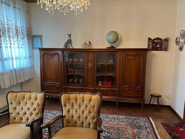 Gemütliches Wohnzimmer mit klassischem Holzschrank, Teppich und Kronleuchter im Vintage-Stil.