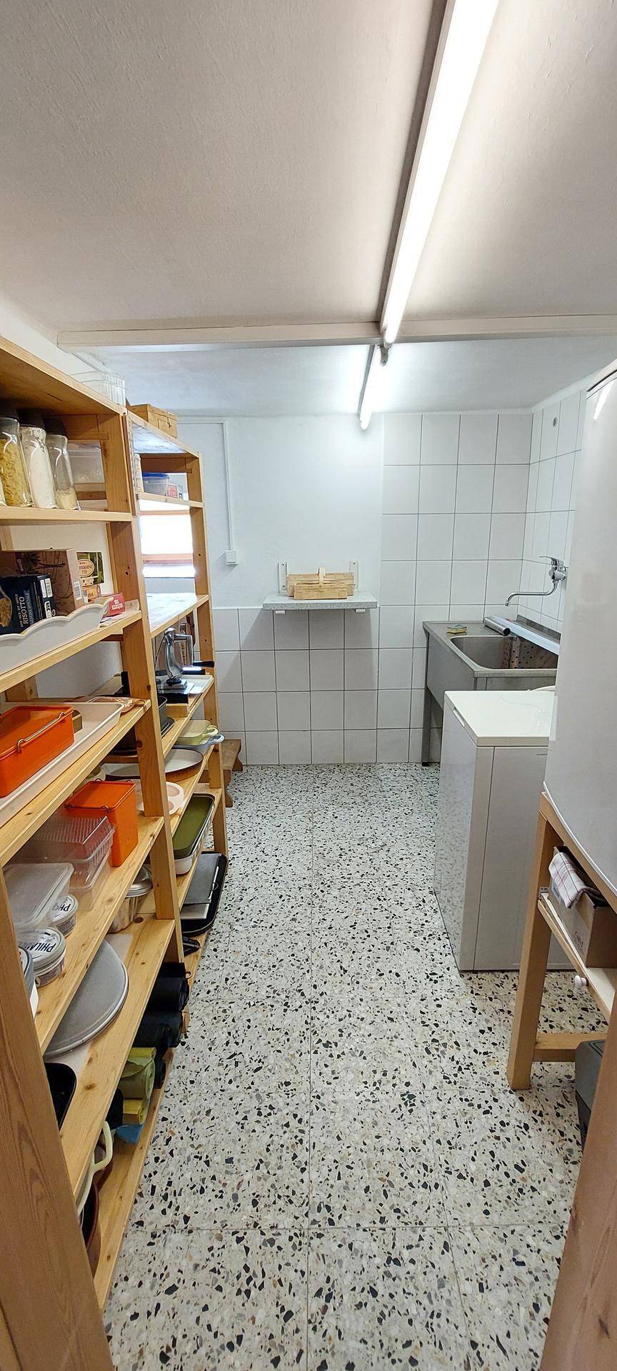 Hauswirtschaftsraum mit Holzregalen, Spüle und Waschmaschine, gefliesten Wänden und Terrazzoboden.