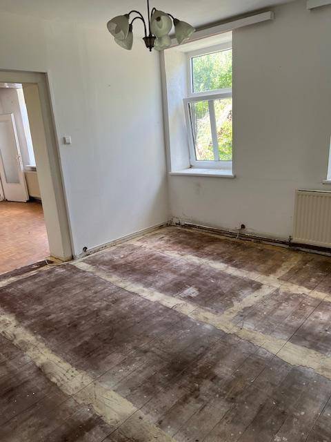 Renovierungsbedürftiger Raum mit beschädigtem Boden, Fenster und Deckenleuchte.