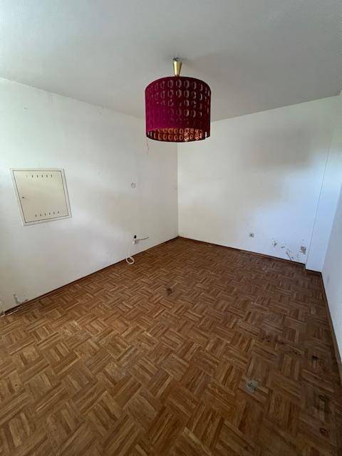 Leerer Raum mit Parkettboden, weißen Wänden und einer roten Deckenlampe.