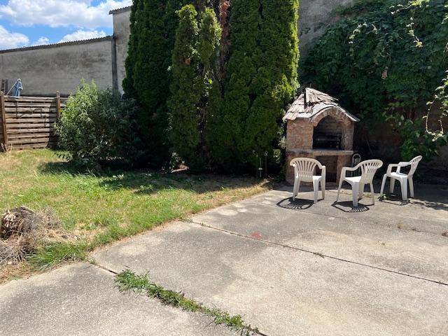 Gepflasterter Terrassenbereich im Garten mit gemauertem Grill und Plastikstühlen.