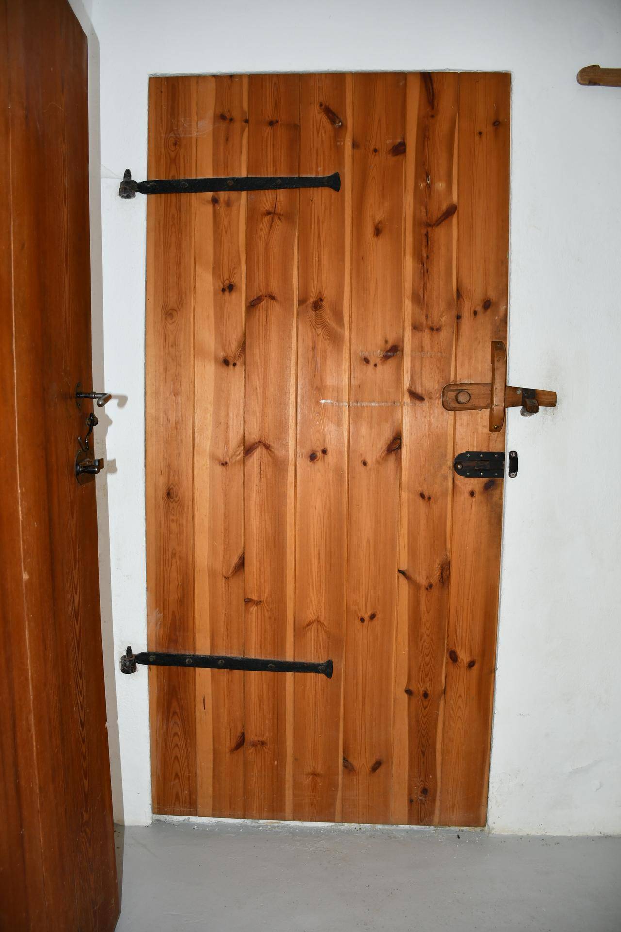 Eine rustikale Holztür mit schwarzen Beschlägen und einem traditionellen Holzriegel, die einen charmanten Eingang bildet.
