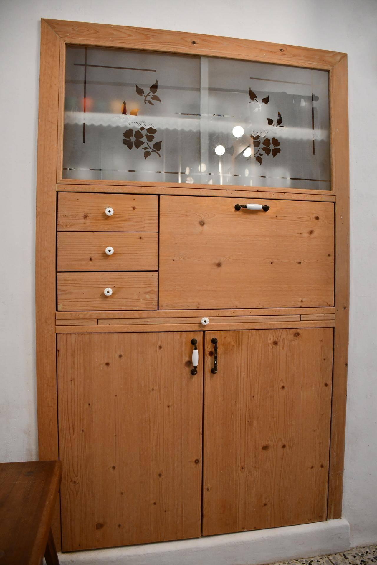 Detailansicht eines eingebauten traditionellen Holzschranks mit verzierten Glastüren und praktischen Schubladen.