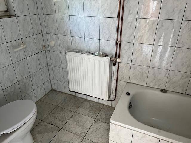 Badezimmer mit weißen Fliesen, Badewanne, Toilette und Heizkörper.