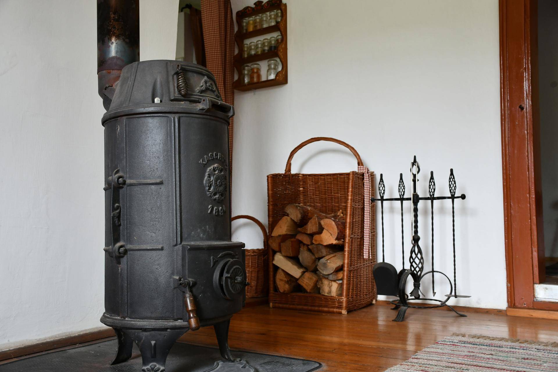 Detailaufnahme eines rustikalen Holzofens mit Brennholzkorb und Kaminbesteck.