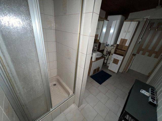 Duschbereich im Badezimmer mit hellen Fliesen und einer einfachen Duschkabine.