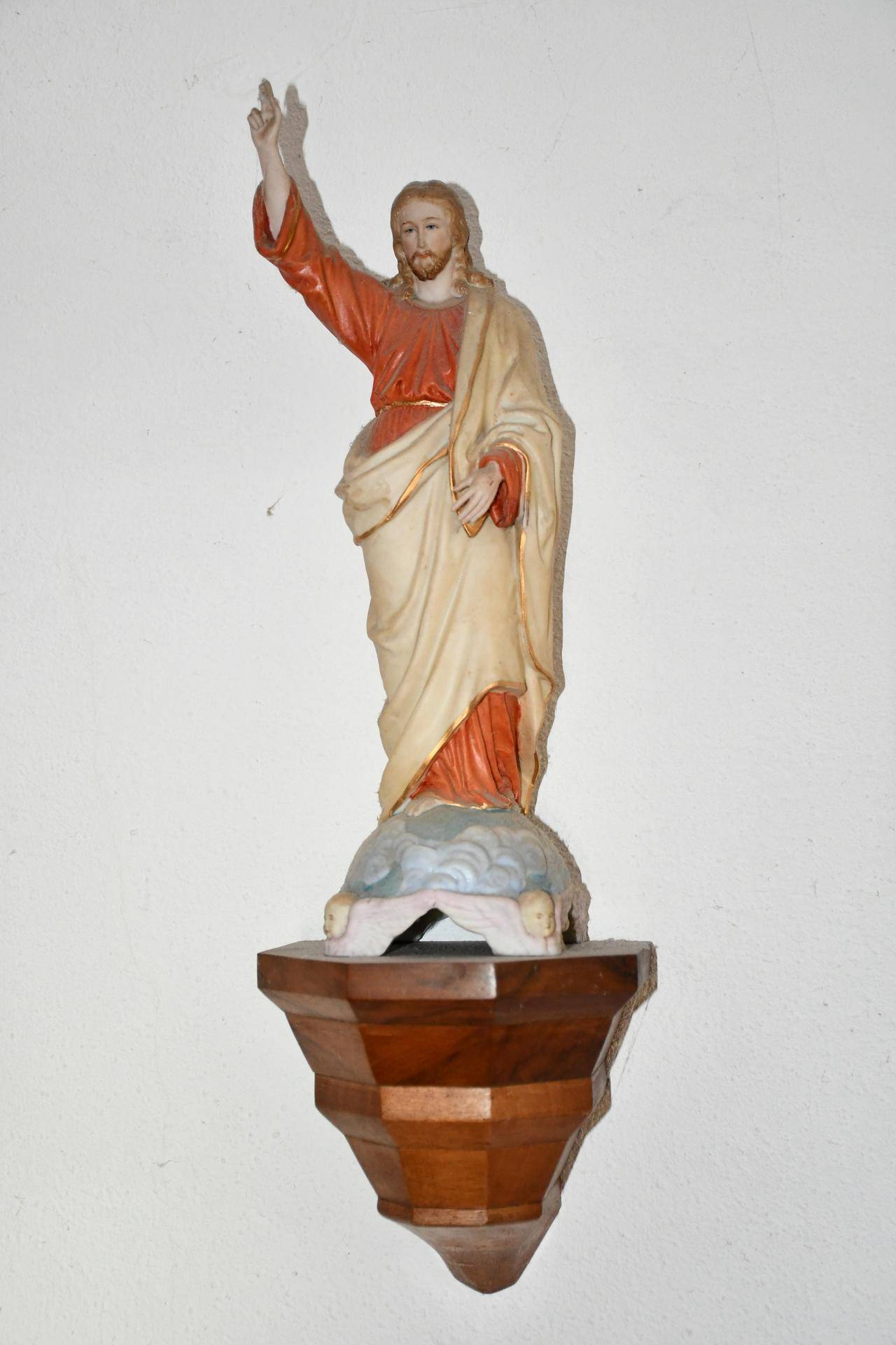 Eine religiöse Statue von Jesus Christus auf einem hölzernen Sockel an einer weißen Wand.