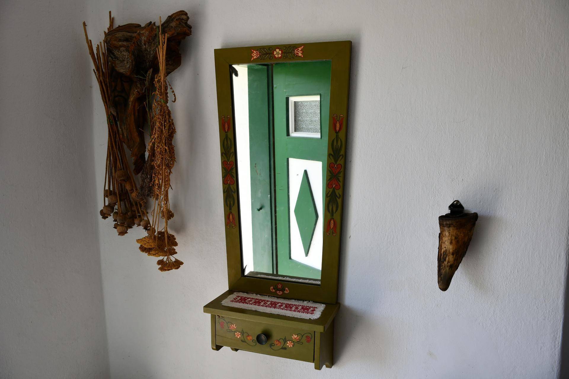 Ein bemalter Holzspiegel mit kleiner Ablage und traditionellen Dekorationen an der Wand.