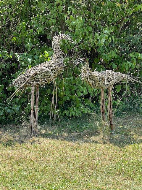 Zwei dekorative Kranichfiguren aus Weidenzweigen in einer grünen Gartenlandschaft.