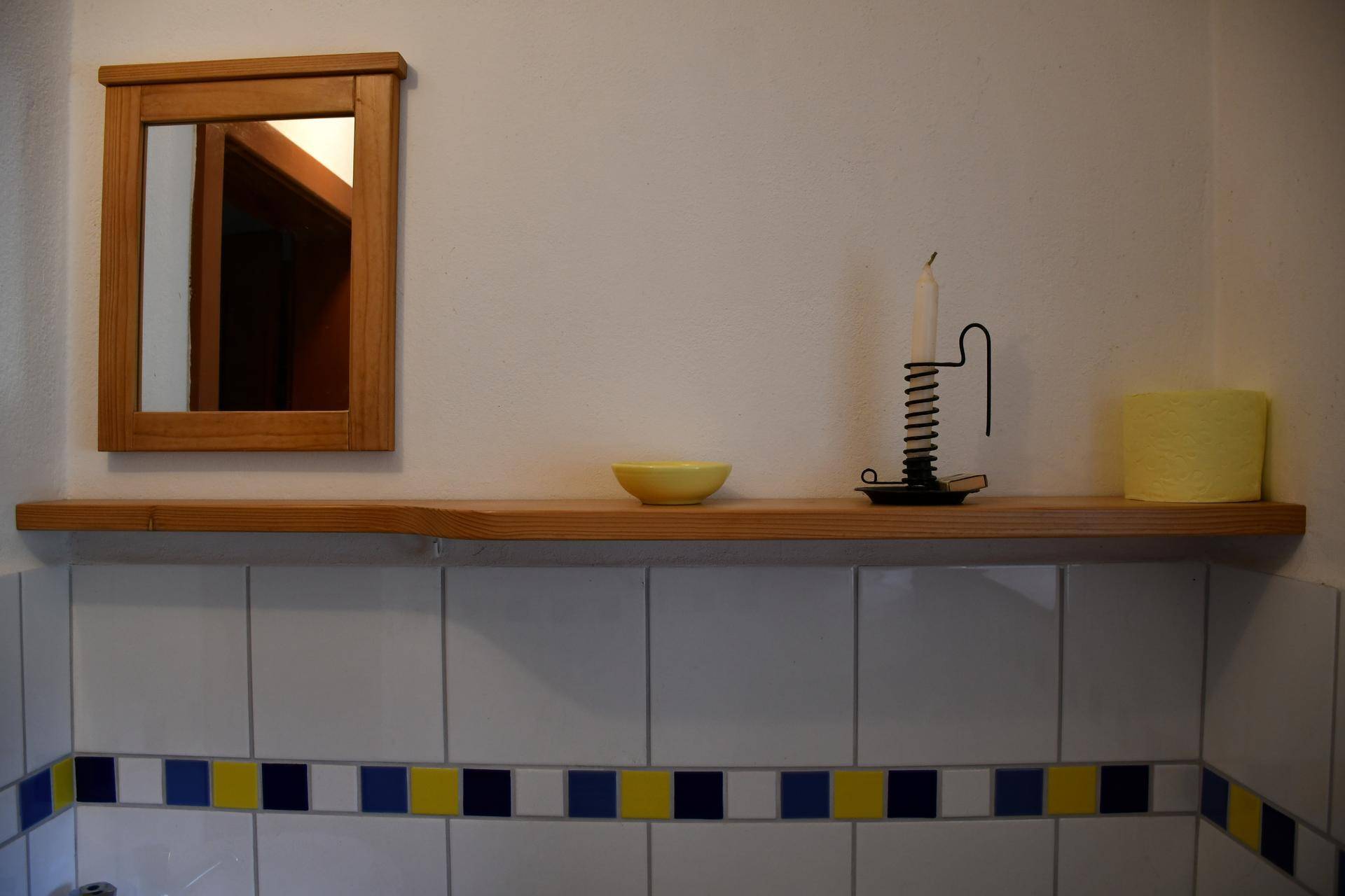 Detailaufnahme eines Holzregals mit Spiegel und traditioneller Dekoration an einer weißen Wand.