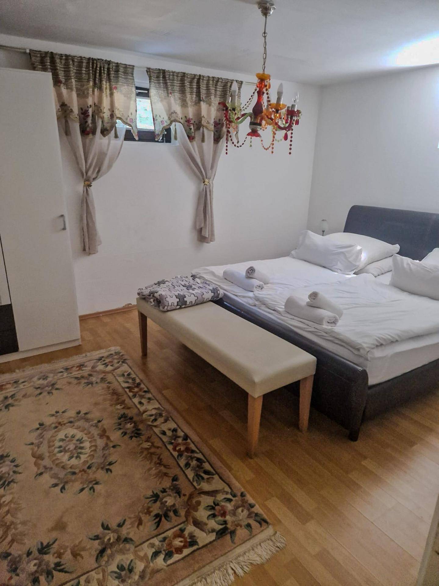 Schlafzimmer mit Doppelbett, Sitzbank und einem dekorativen Kronleuchter, ausgestattet mit Holzboden.