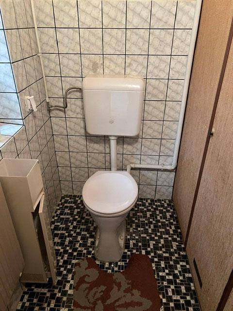 Separate Toilette mit Fliesen an Wänden und Boden im 80er-Jahre-Stil.