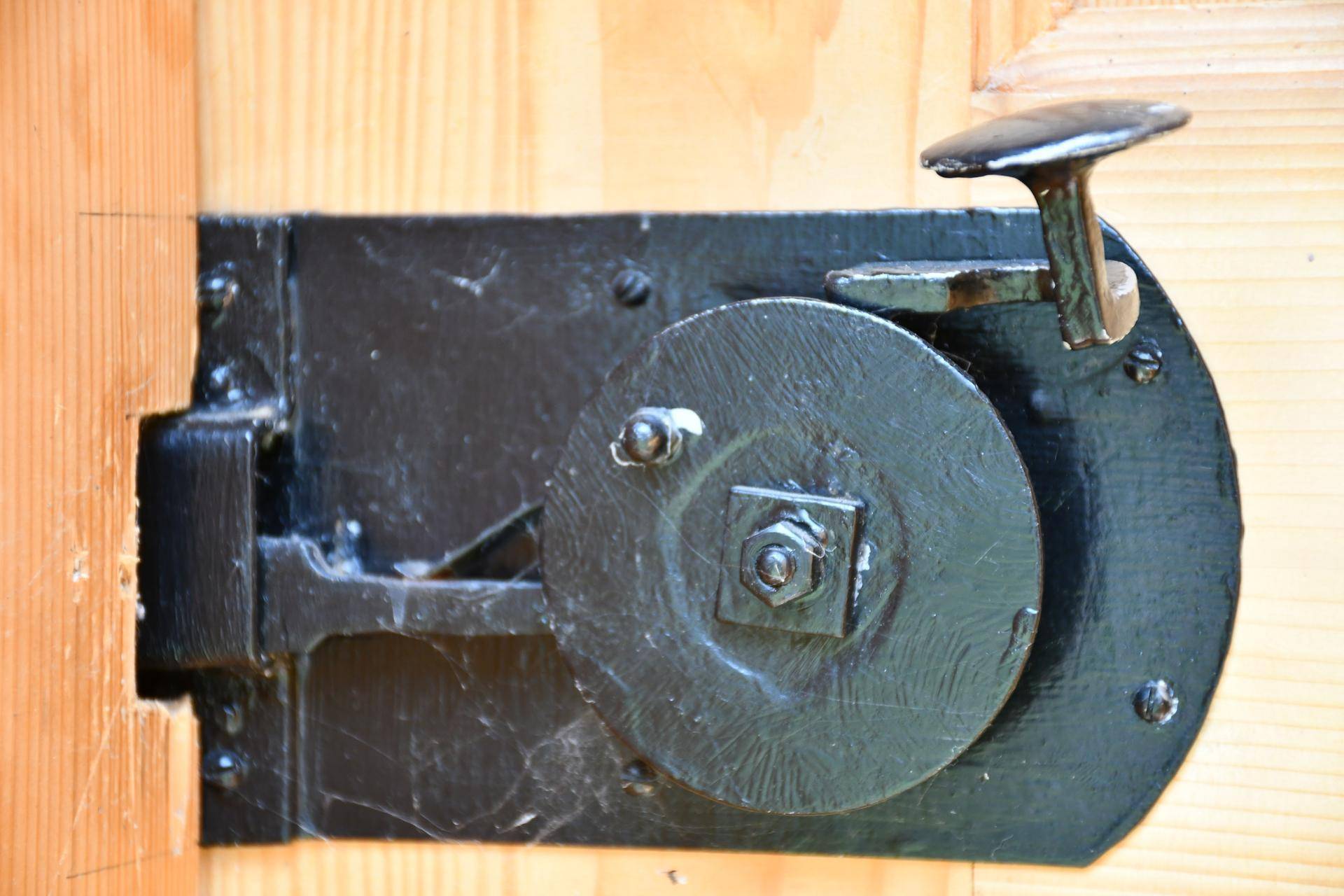 Nahaufnahme eines alten, runden Türschlosses aus schwarzem Metall an einer hellen Holztür.