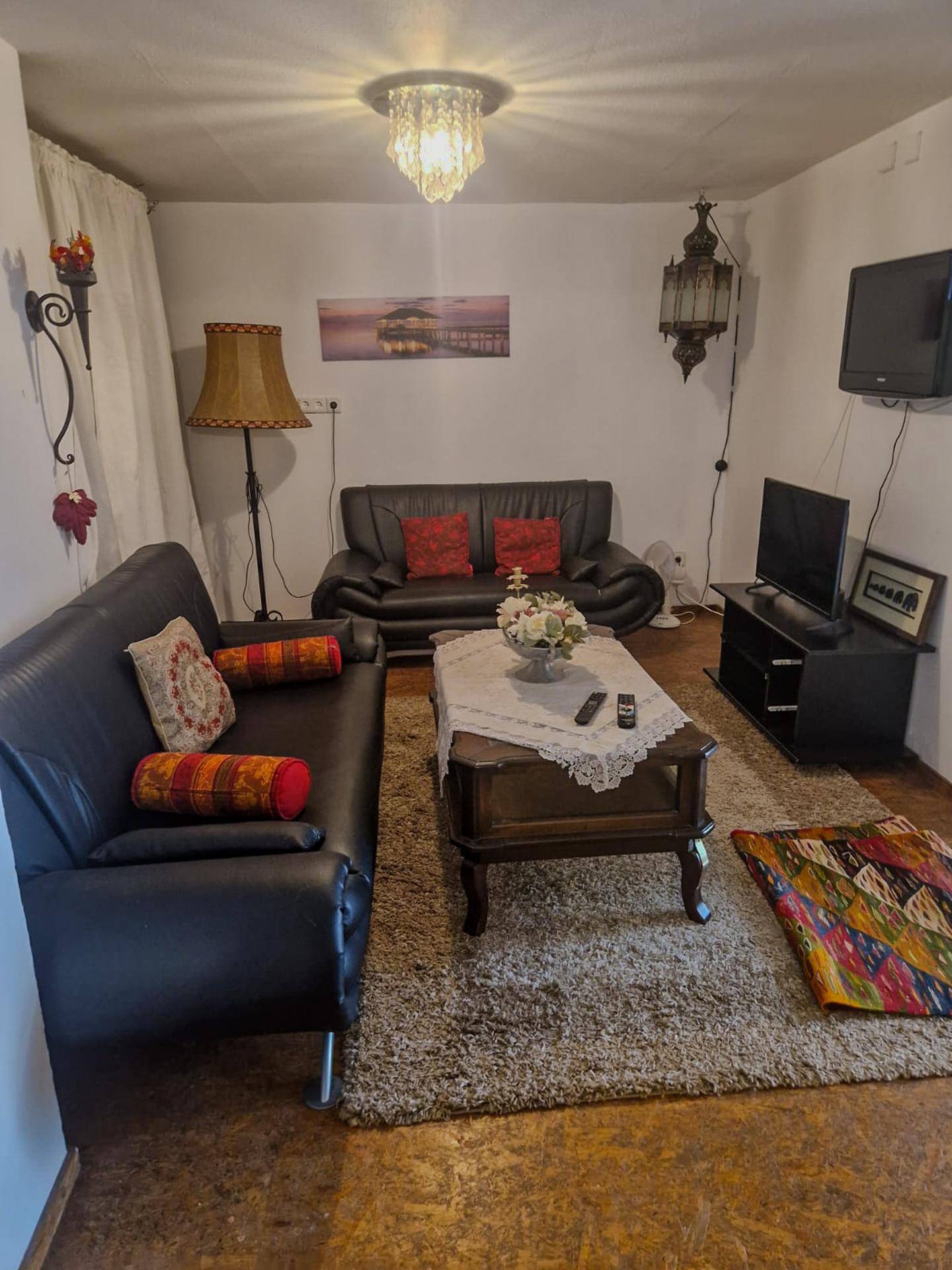 Gemütliches Wohnzimmer mit zwei schwarzen Sofas, Couchtisch und Fernseher, auf einem flauschigen Teppich.