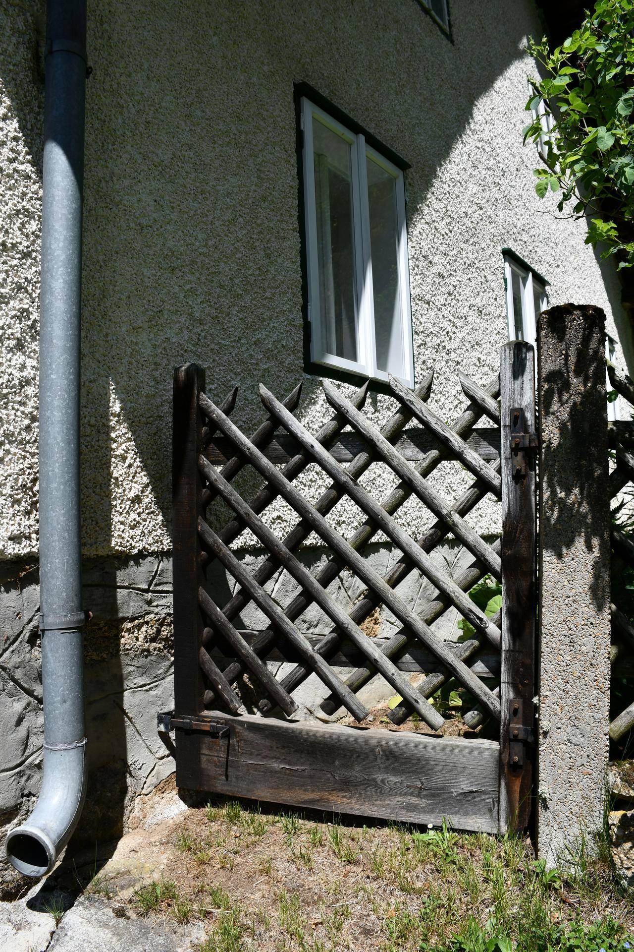 Detailansicht eines rustikalen Holzzauns und der Hauswand mit Fallrohr.