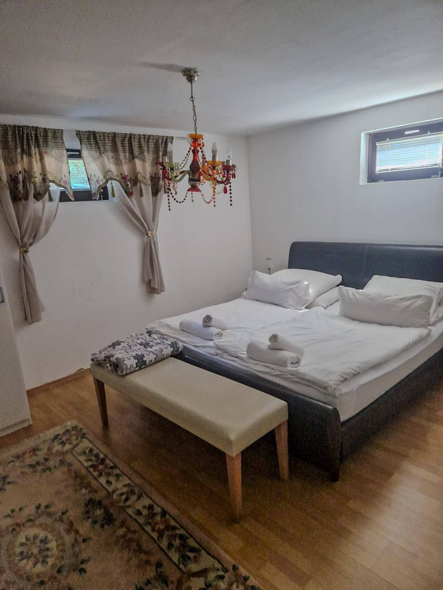 Schlafzimmer mit Doppelbett, Sitzbank und einem dekorativen Kronleuchter, ausgestattet mit Holzboden.