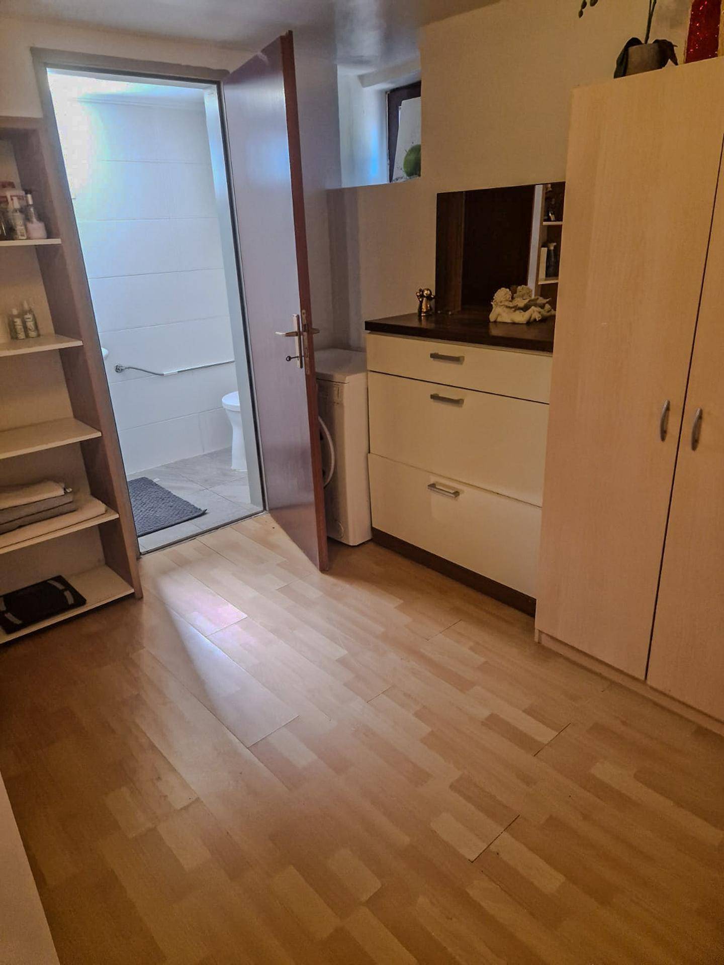 Heller Flur mit Laminatboden und Blick in ein Badezimmer mit Toilette und Haltegriff.