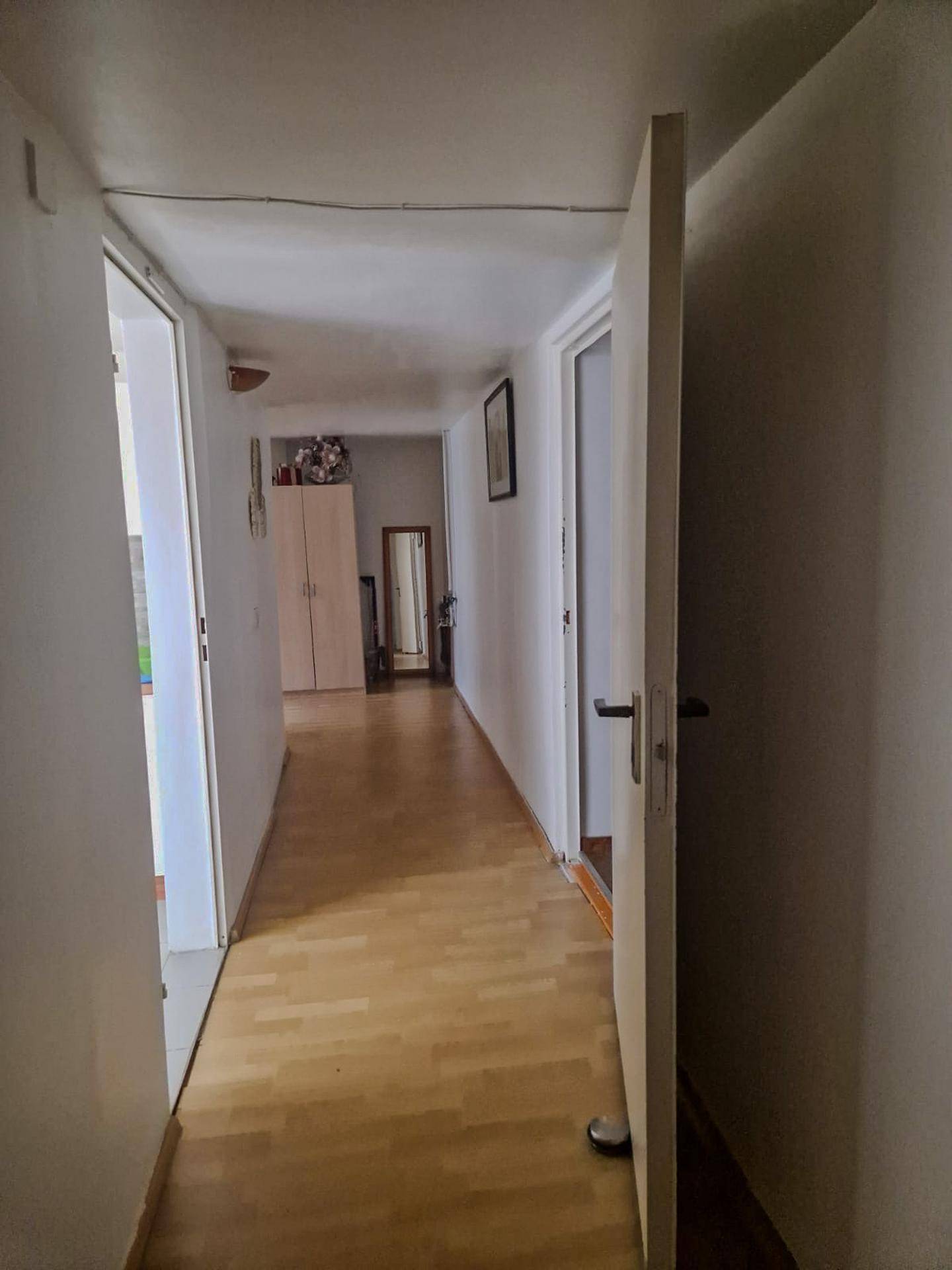 Langer, heller Flur mit Laminatboden und mehreren Türen, der zu weiteren Räumen führt.