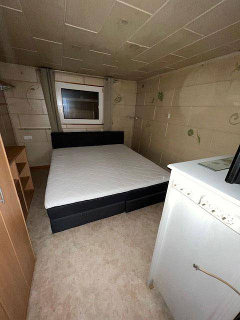 Schlafzimmer mit Doppelbett, einfacher Einrichtung und einem kleinen Fenster.