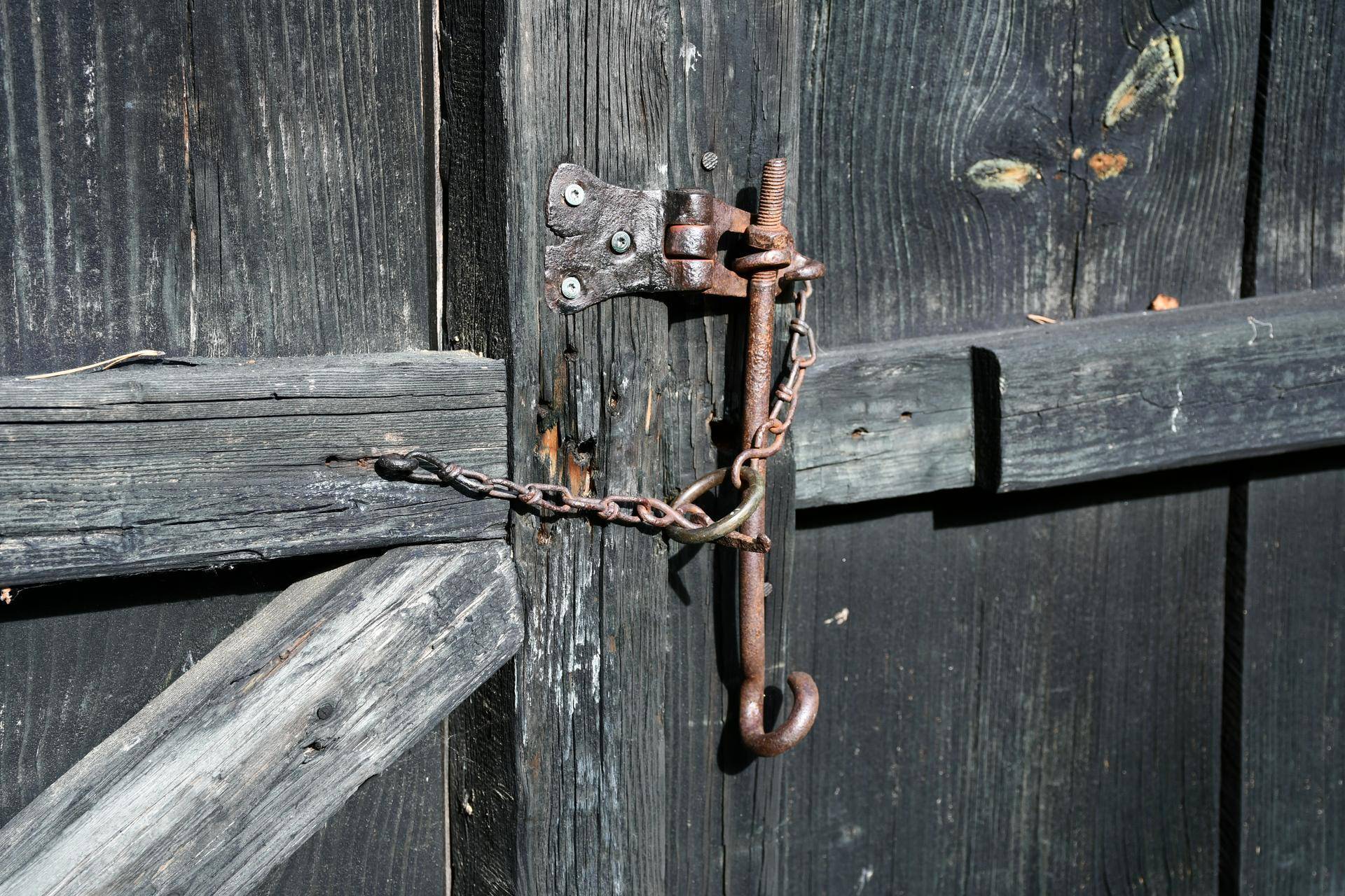 Detailaufnahme eines rustikalen Metallriegels mit Kette an einer alten Holztür.