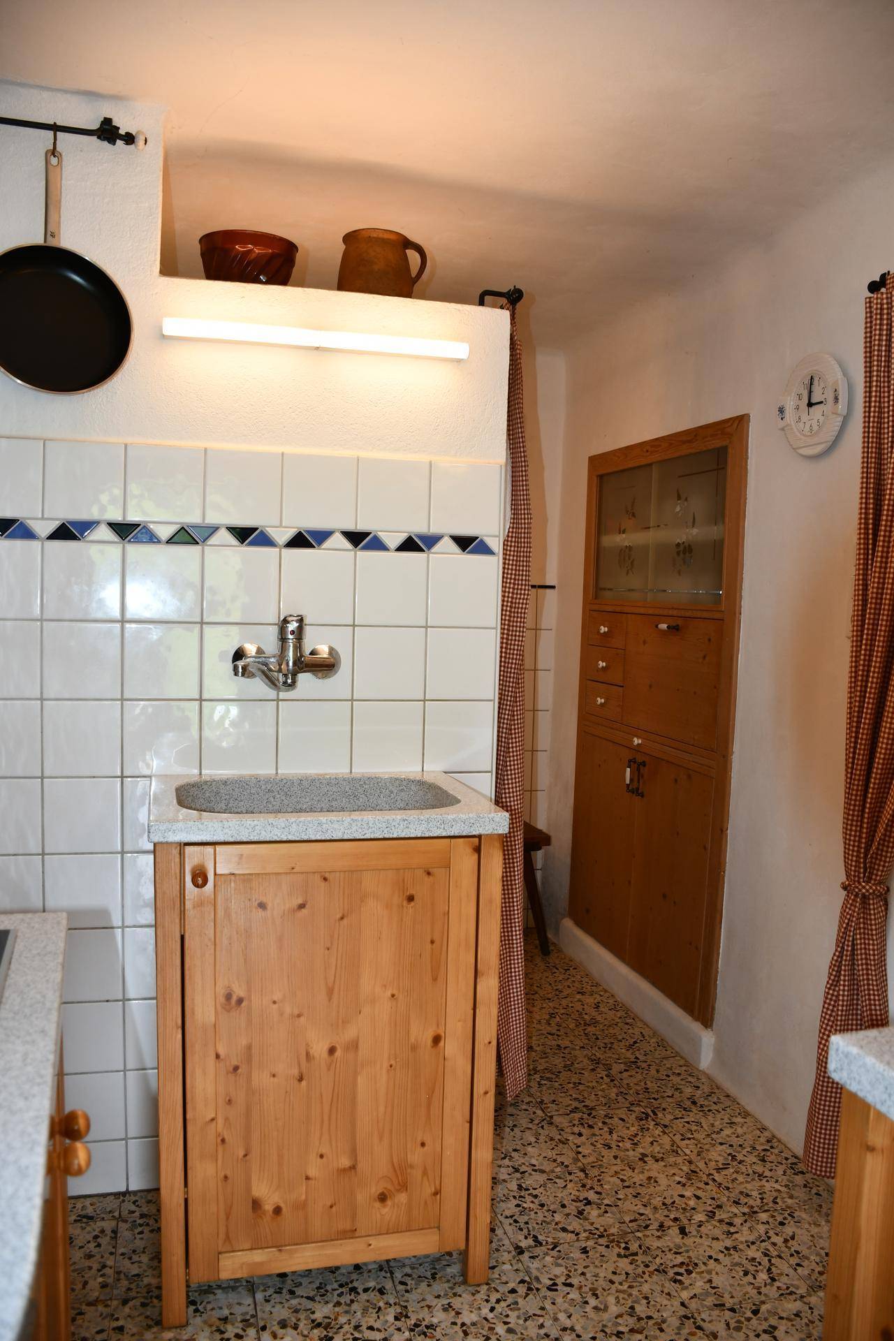 Küchenecke mit Steinsspüle, Holzschrank und gefliesten Wänden, ergänzt durch einen eingebauten Holzschrank.