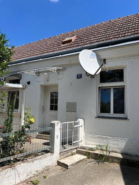 Vorderansicht eines weißen Hauses mit Satellitenschüssel, Fenstern und einem kleinen Zaun.
