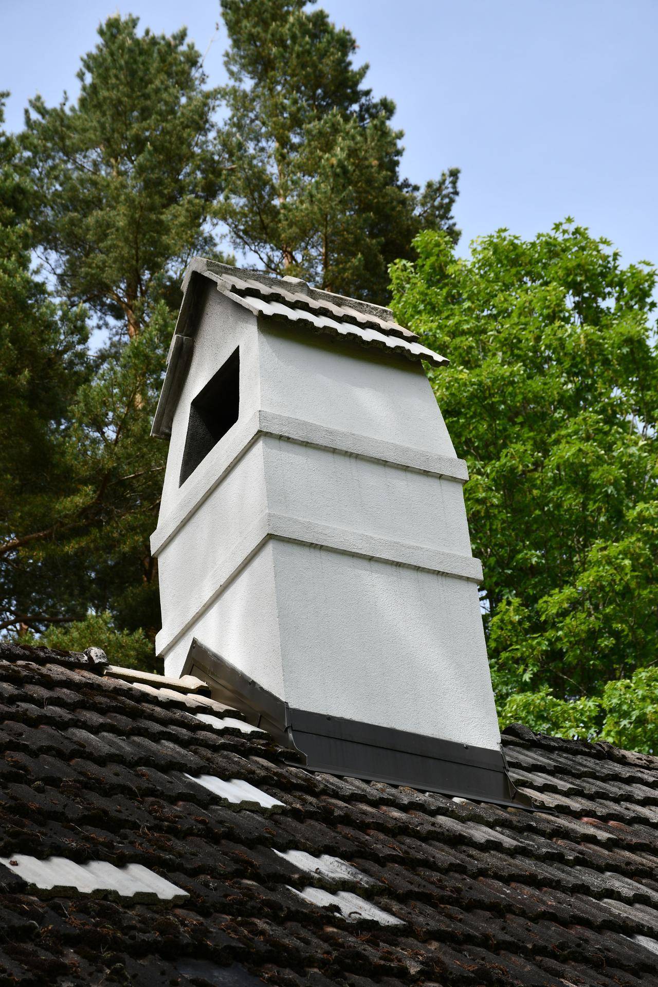 Nahaufnahme eines weißen Kamins auf einem traditionellen Ziegeldach unter blauem Himmel.