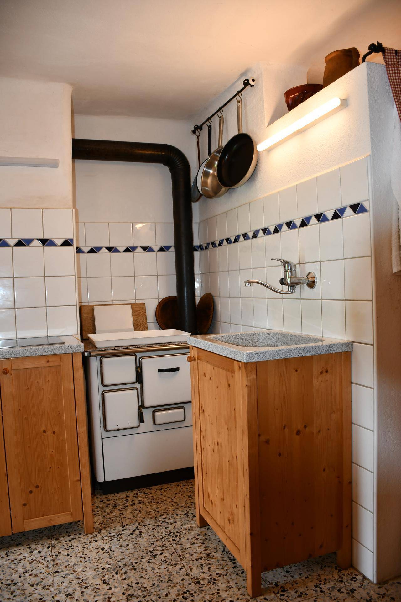 Traditionelle Küche mit Holzofen, weißen Fliesen und blauen Akzenten, sowie rustikalen Holzschränken.