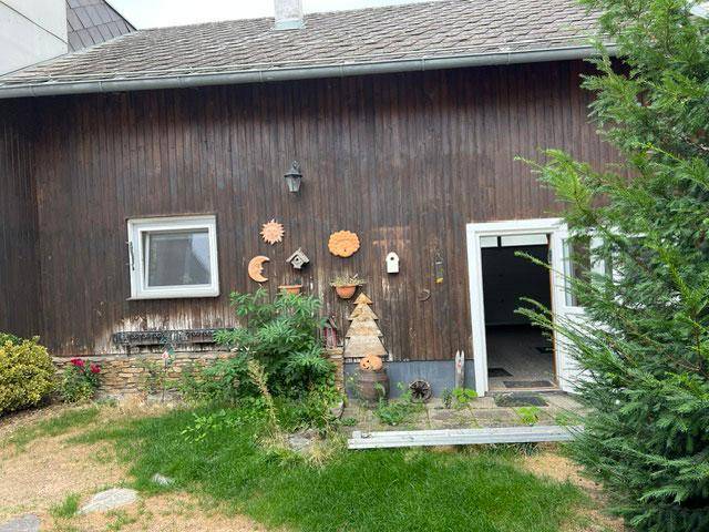 Hinterhof mit Holzwand, Fenster und Tür, umgeben von Grünflächen.