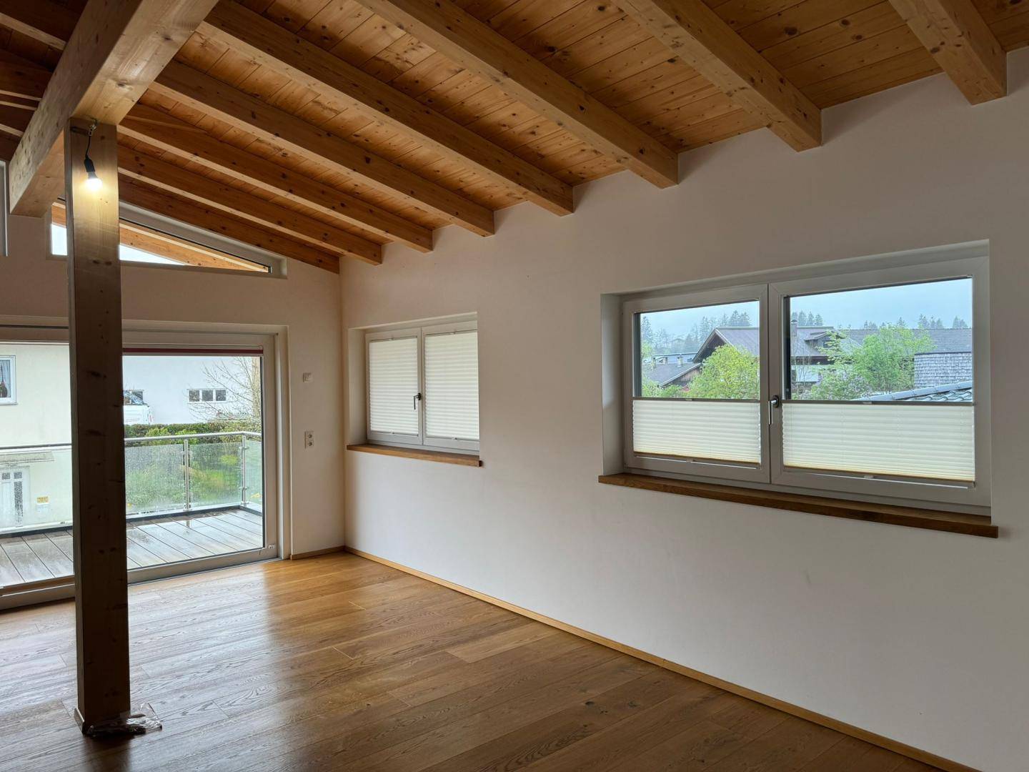 Heller Raum mit Holzbalkendecke, Parkettboden und Zugang zu einem Balkon mit Aussicht.