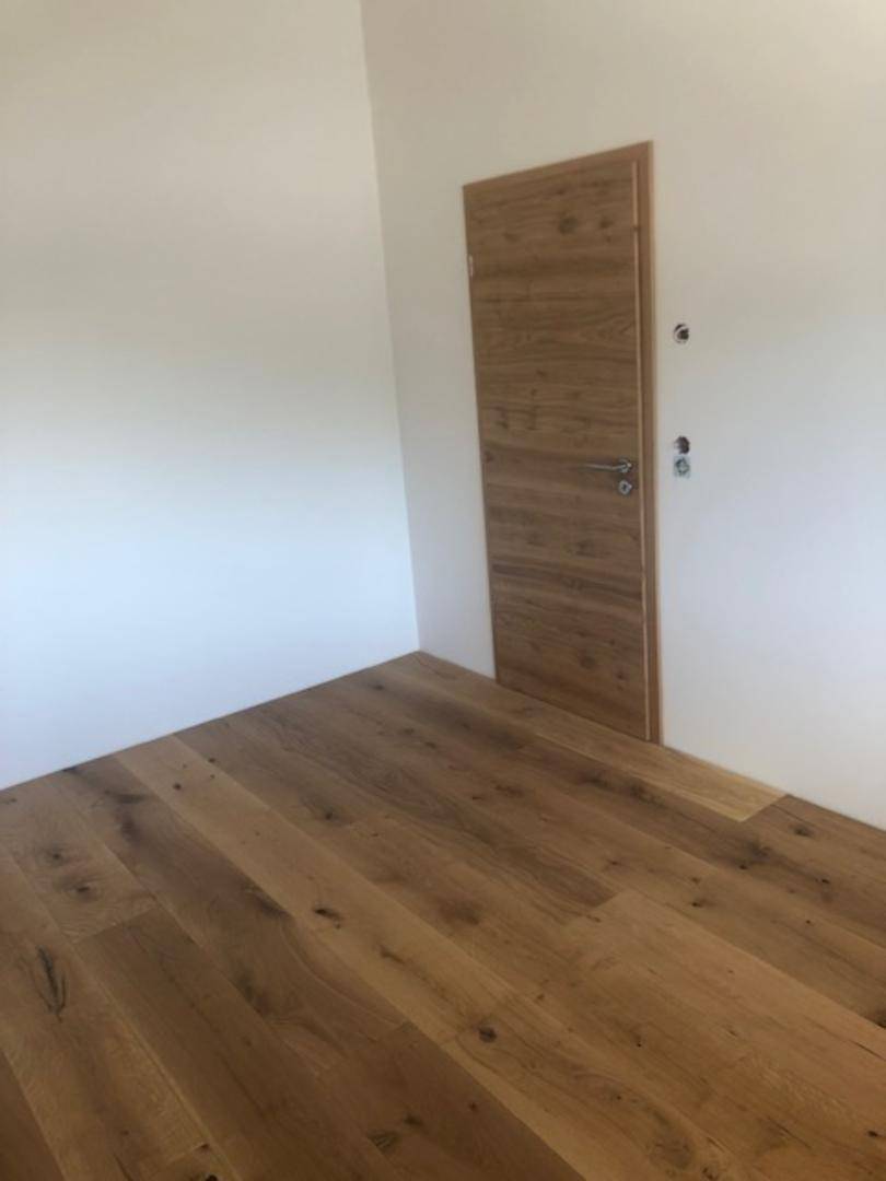 Leerer Raum mit Holztür und hochwertigem Parkettboden, bereit zur individuellen Gestaltung.