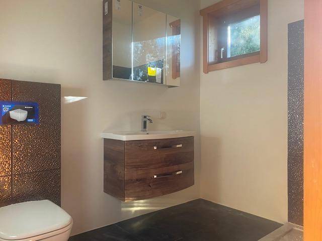 Modernes Badezimmer mit Einzelwaschbecken, Spiegelschrank und dunklen Akzentfliesen.