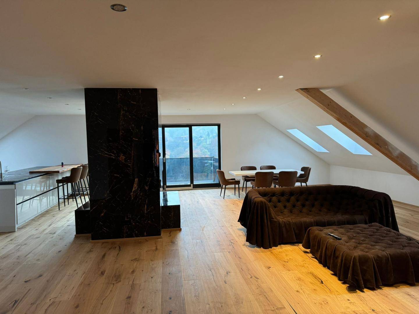 Geräumiger offener Wohn-Essbereich mit Marmorkamin, Holzboden und Zugang zu einem Balkon.
