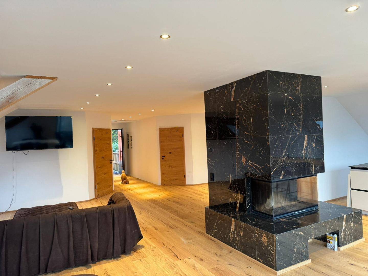 Helles Wohnzimmer mit modernem Marmorkamin, Holzboden und Zugang zu weiteren Räumen.