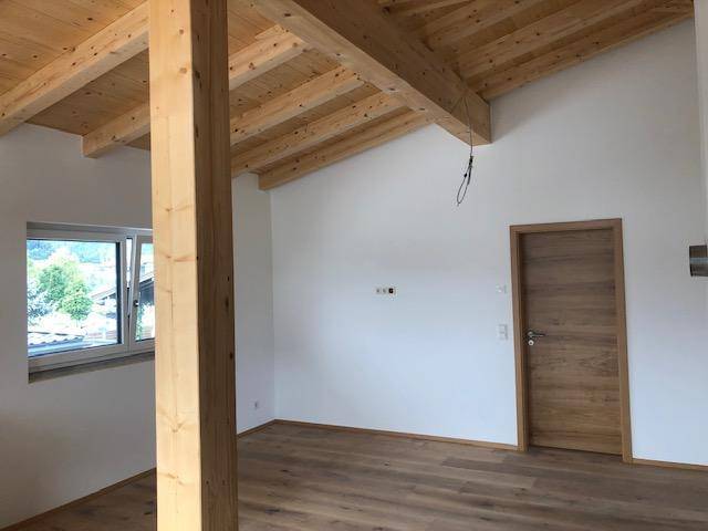Heller Raum mit sichtbaren Holzbalken, Holzboden und einem Fenster mit Ausblick.