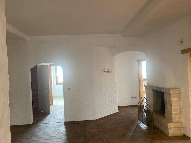 Geräumiges Wohnzimmer mit weiß getünchten Wänden, rustikalem Kamin und Terrakotta-Fliesenboden.