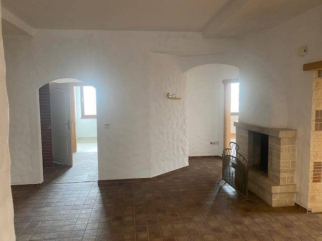 Wohnzimmer mit Terrakottafliesen, strukturierten weißen Wänden, Rundbögen und einem gemauerten Kamin.