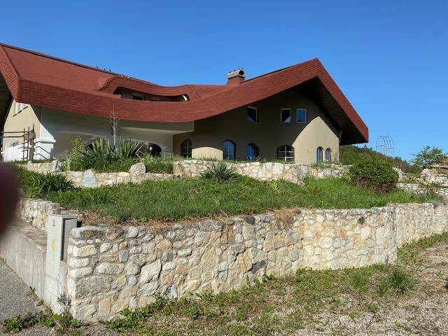 Das Haus mit seiner einzigartigen Architektur und der Natursteinmauer, umgeben von spärlicher Vegetation.