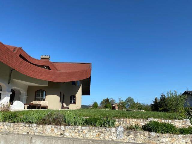 Seitenansicht des Hauses mit weitläufiger Rasenfläche und dem geschwungenen Dach unter blauem Himmel.