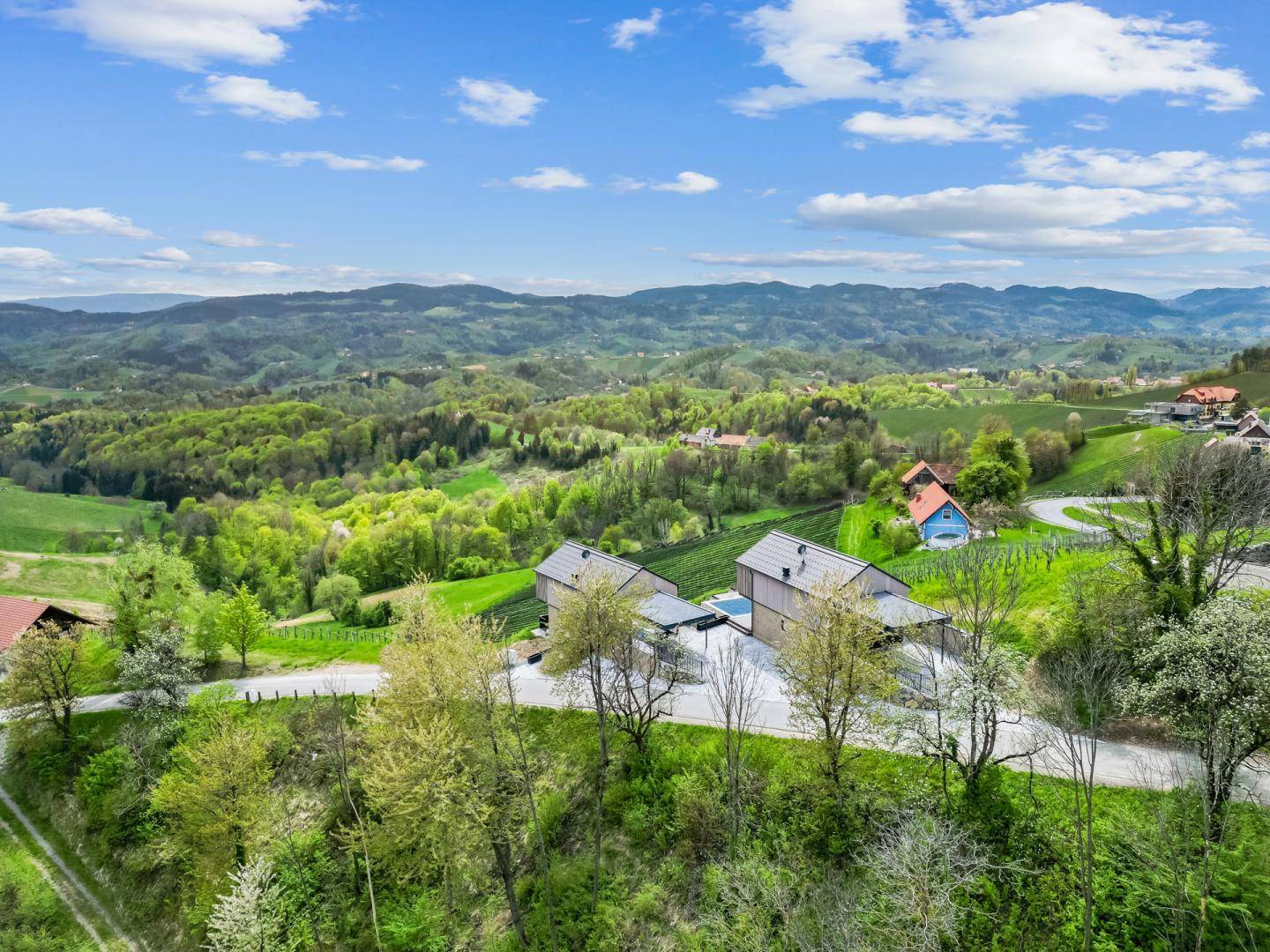 Weitläufige Luftaufnahme der modernen Häuser in einer grünen, hügeligen Landschaft mit Weinbergen.