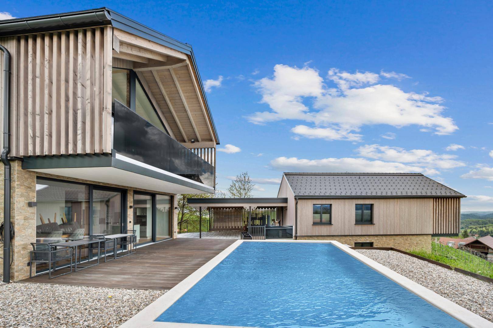 Großer Poolbereich mit Holzterrasse und Essbereich im Freien, umgeben von moderner Architektur.